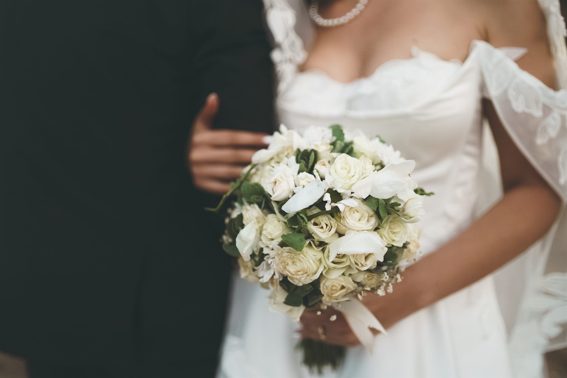 A bride holds a white bouquet close, soft daylight across lace